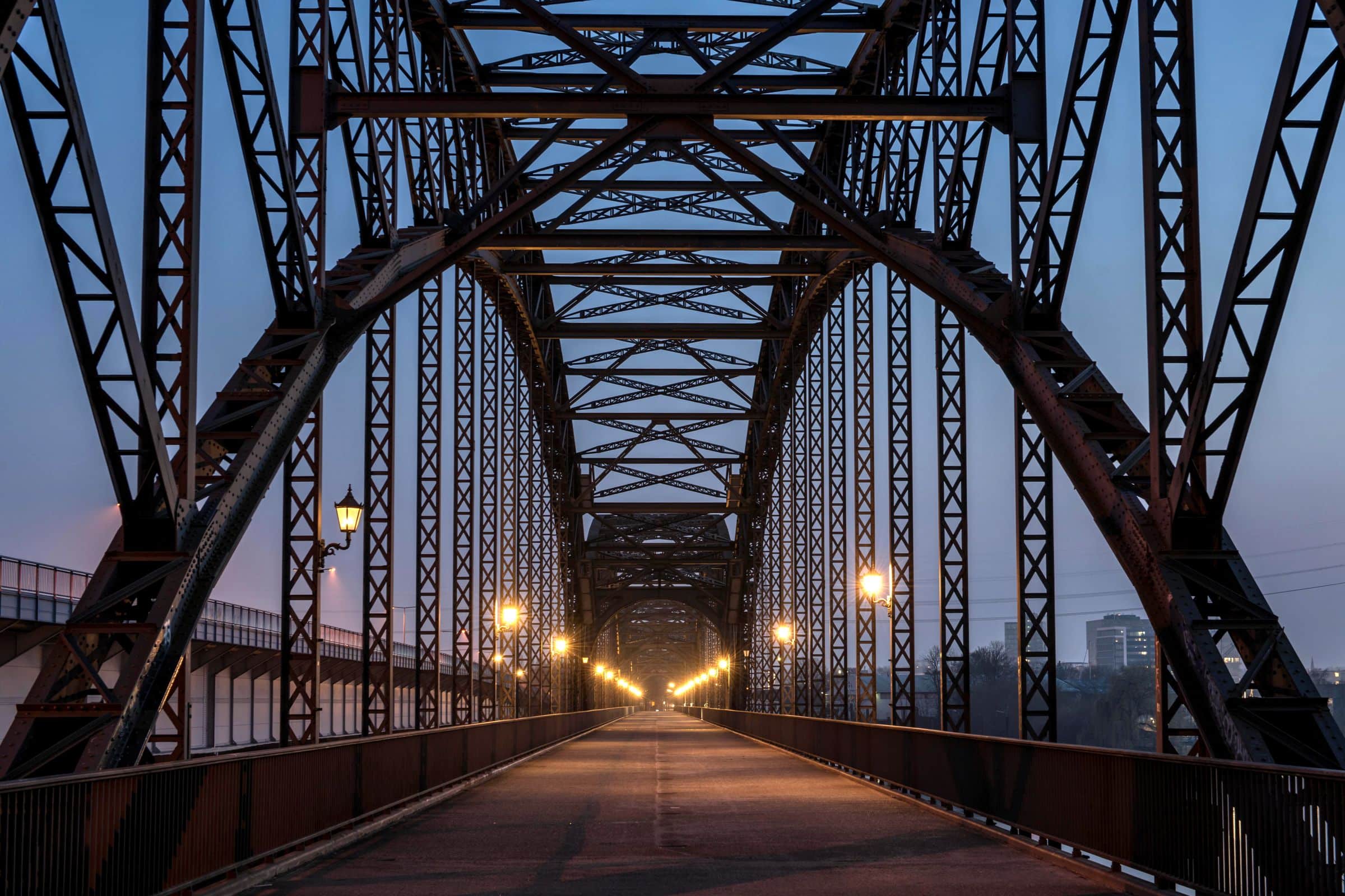Alte Stahlbrücke mit leuchtenden Laternen in der blauen Stunde, Blick tief in die Brücke hinein